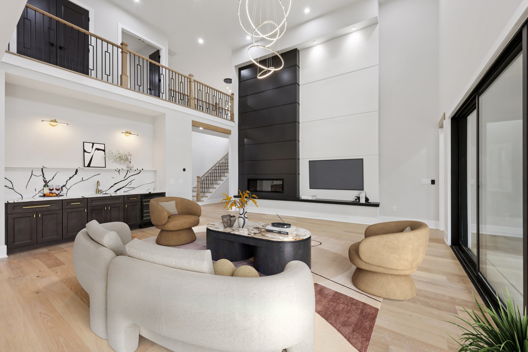 Great room with a two-story black fireplace, floating wet bar, and open upstairs loft, staged